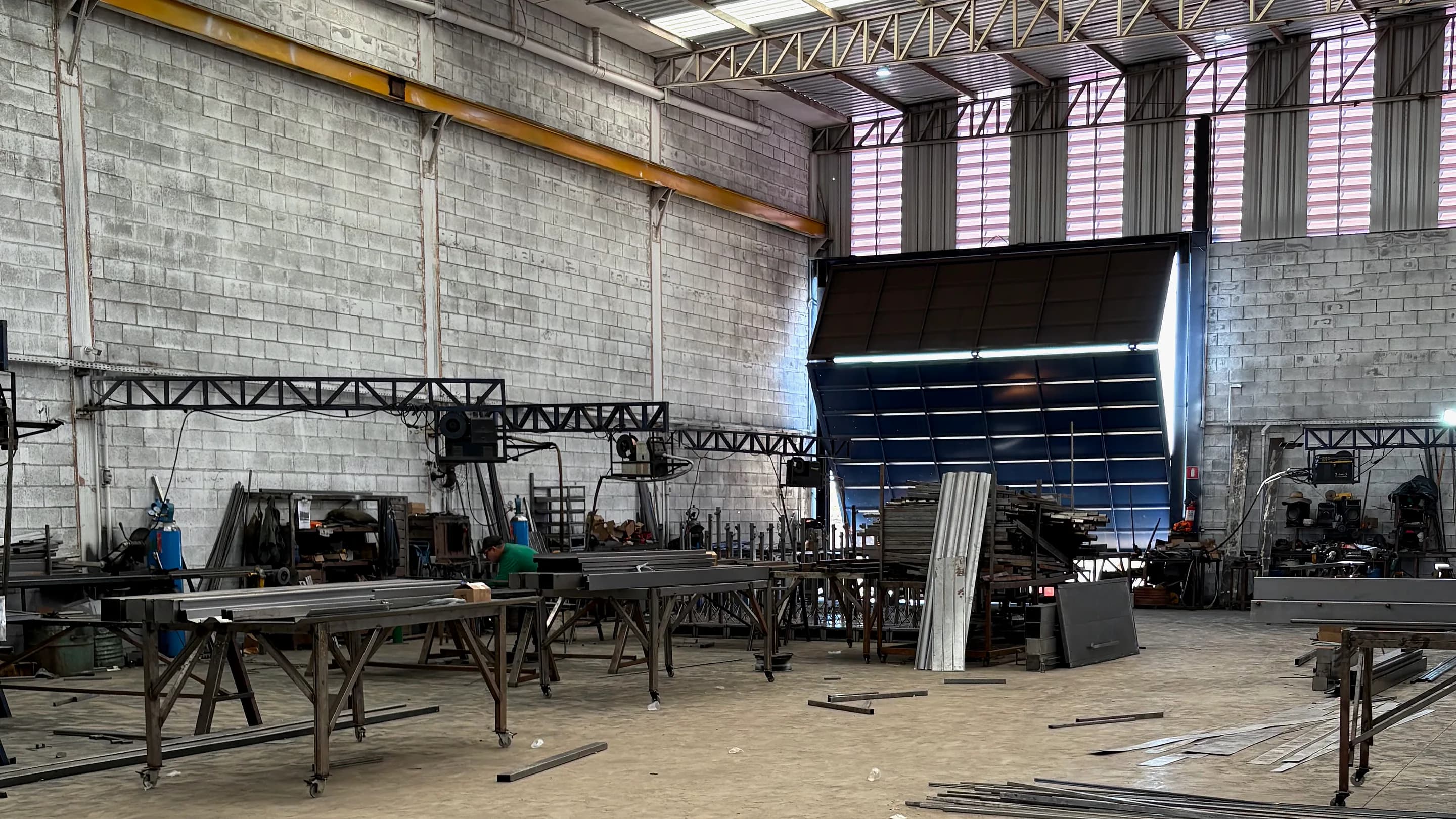 Galpão de produção da Portões Rio Preto com cobertura metálica, bancadas de montagem e o portão de carga ao fundo