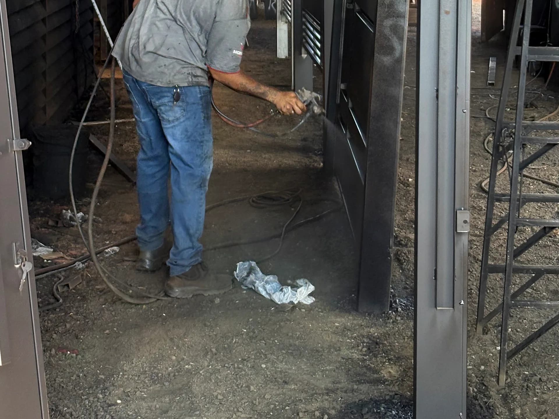 Pintor aplicando fundo primer anticorrosivo com pistola em um portão, na área de pintura da fábrica