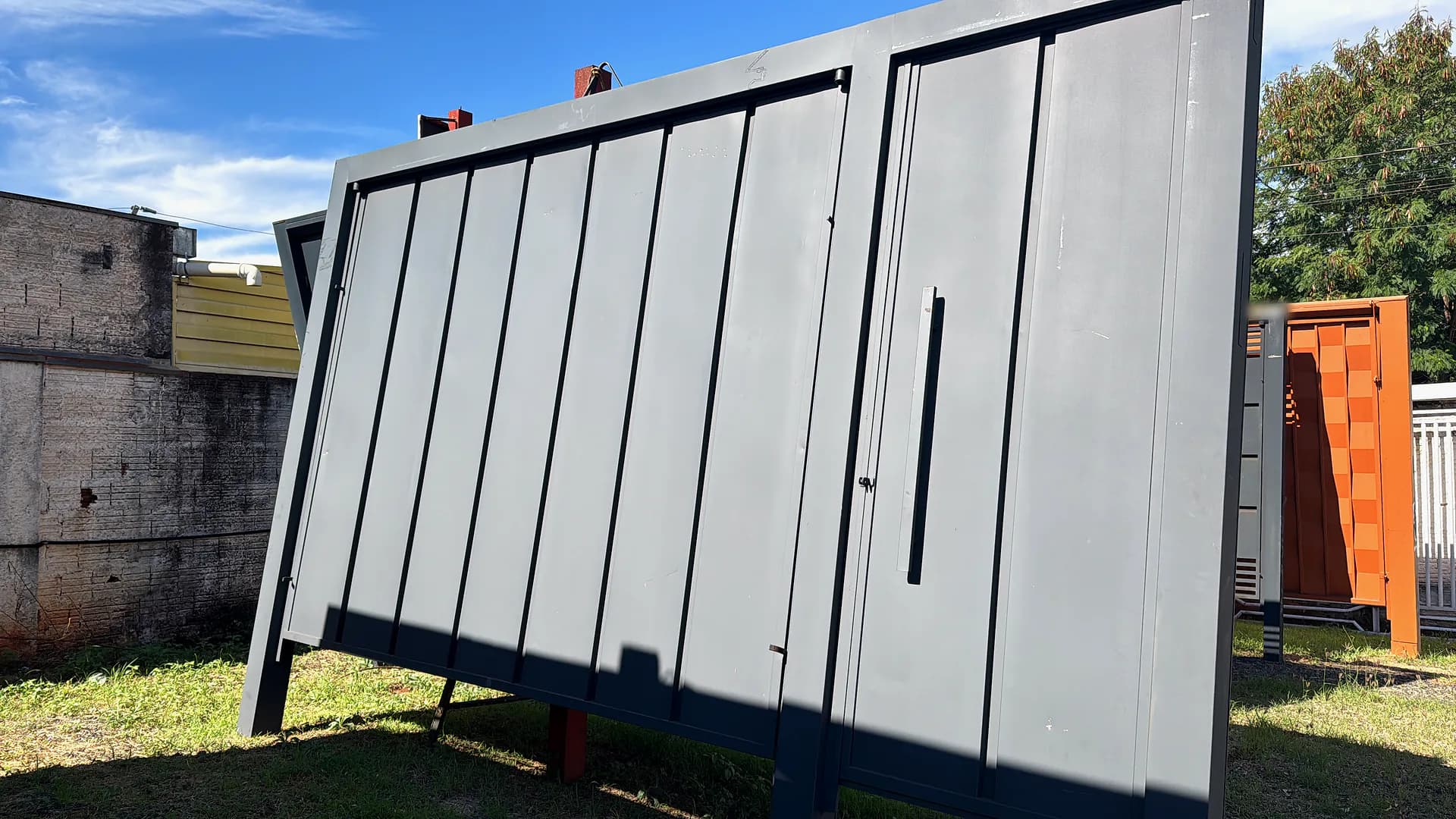 Portão basculante cinza com frisos e porta social no pátio da fábrica